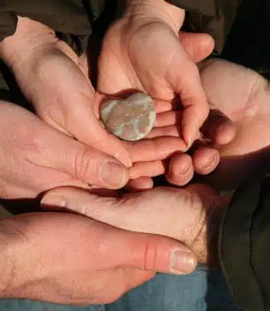 Several hands gently cradle a single smooth, round stone, symbolizing connection and care among the individuals.