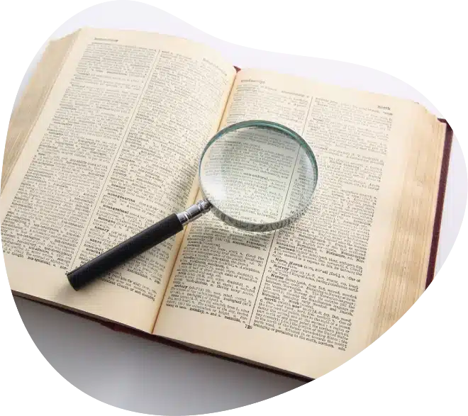 An open dictionary with a magnifying glass resting on its pages, highlighting the text.